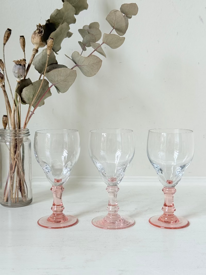 Set of three vintage liquor glasses with clear bowls and pink stems, one paler in tone, photographed on white surface.