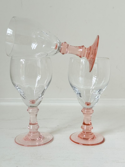 Set of three vintage liquor glasses with clear bowls and pink stems, one paler in tone, photographed on white surface.