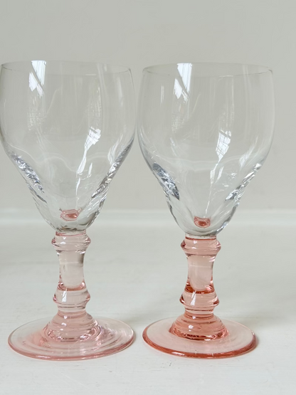 Set of three vintage liquor glasses with clear bowls and pink stems, one paler in tone, photographed on white surface.