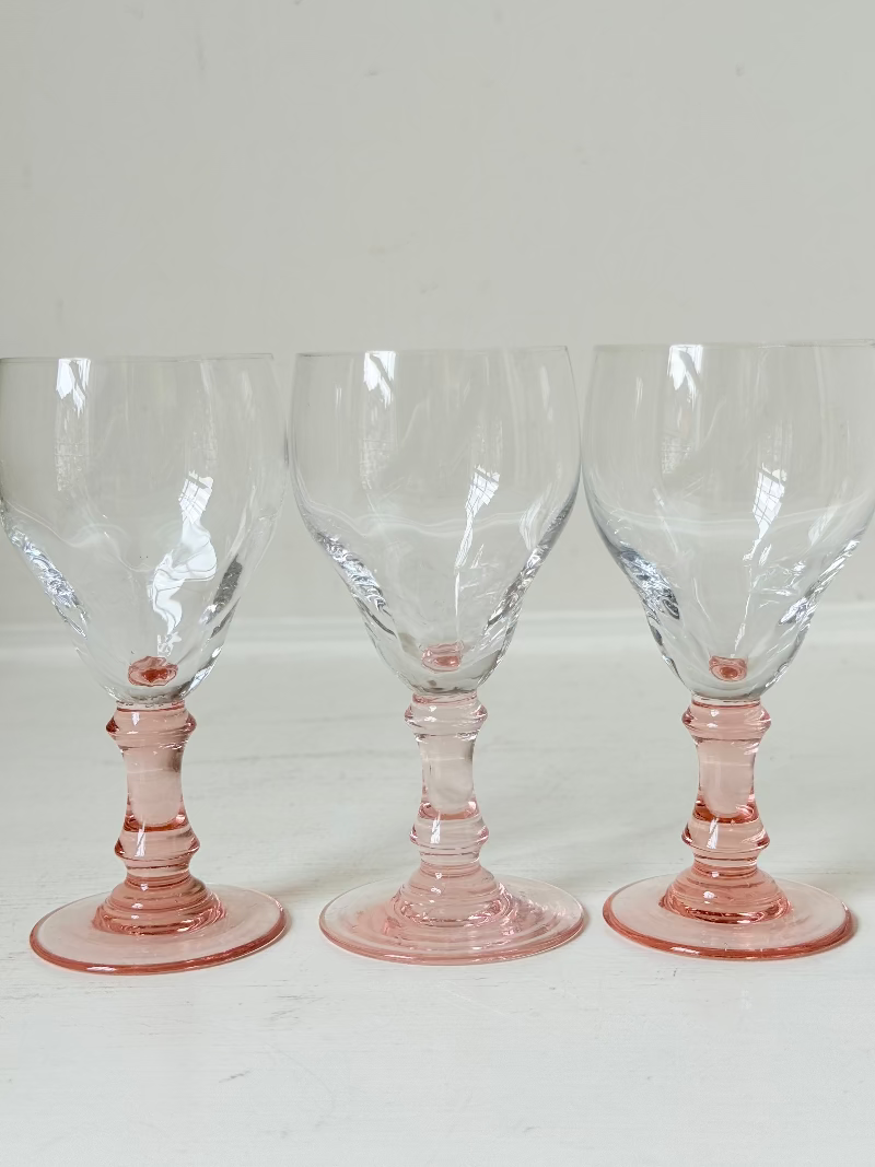 Set of three vintage liquor glasses with clear bowls and pink stems, one paler in tone, photographed on white surface.