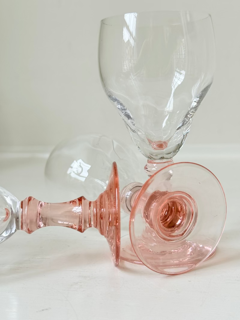Set of three vintage liquor glasses with clear bowls and pink stems, one paler in tone, photographed on white surface.