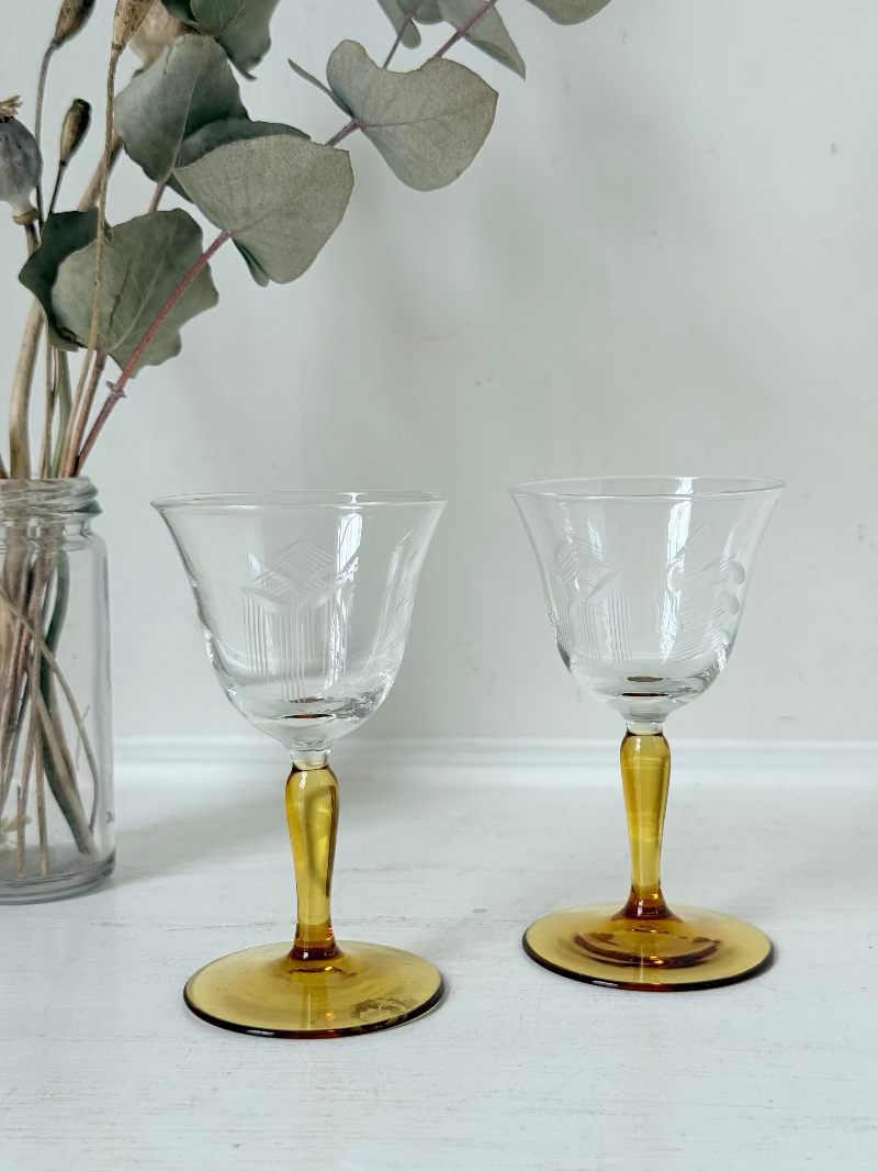 Pair of vintage liquor glasses with clear bowls and amber stems, photographed on white surface.