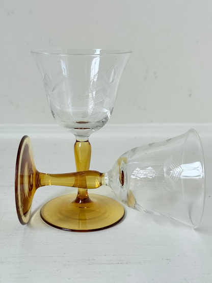 Pair of vintage liquor glasses with clear bowls and amber stems, photographed on white surface.