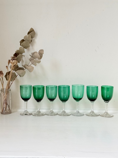 Set of seven antique Bristol green glasses with clear stems and emerald bowls, photographed on white surface.