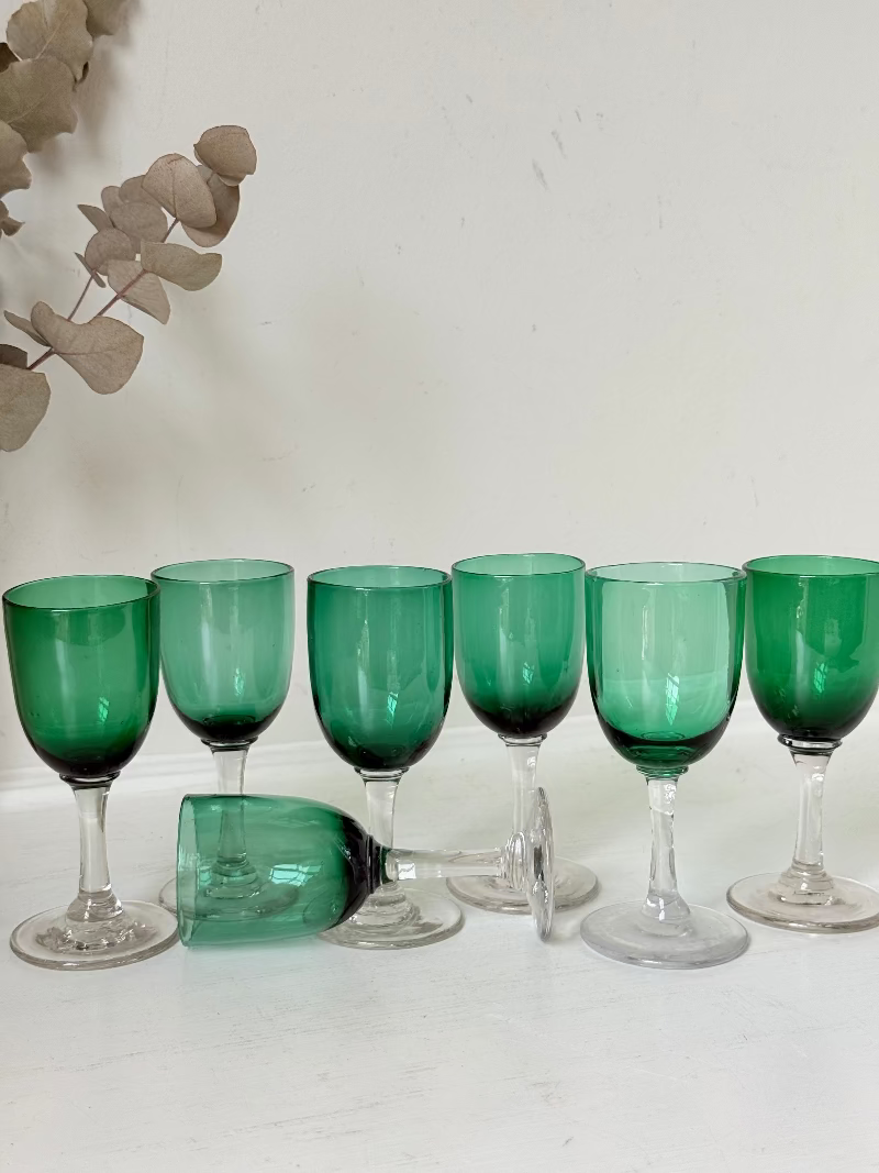 Set of seven antique Bristol green glasses with clear stems and emerald bowls, photographed on white surface.