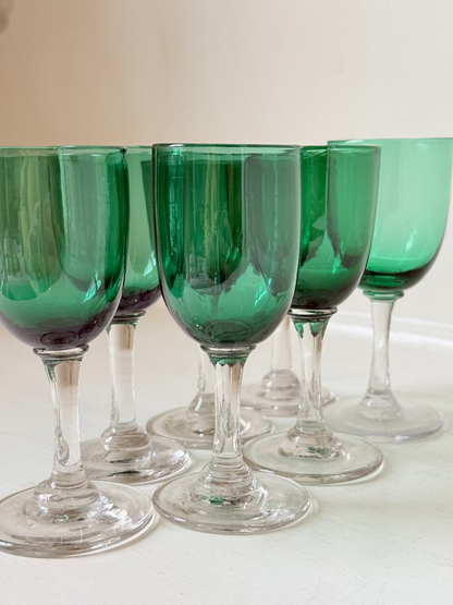 Set of seven antique Bristol green glasses with clear stems and emerald bowls, photographed on white surface.