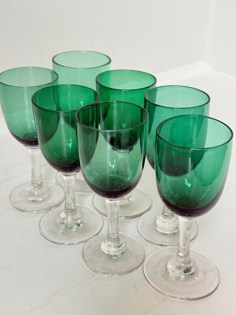 Set of seven antique Bristol green glasses with clear stems and emerald bowls, photographed on white surface.