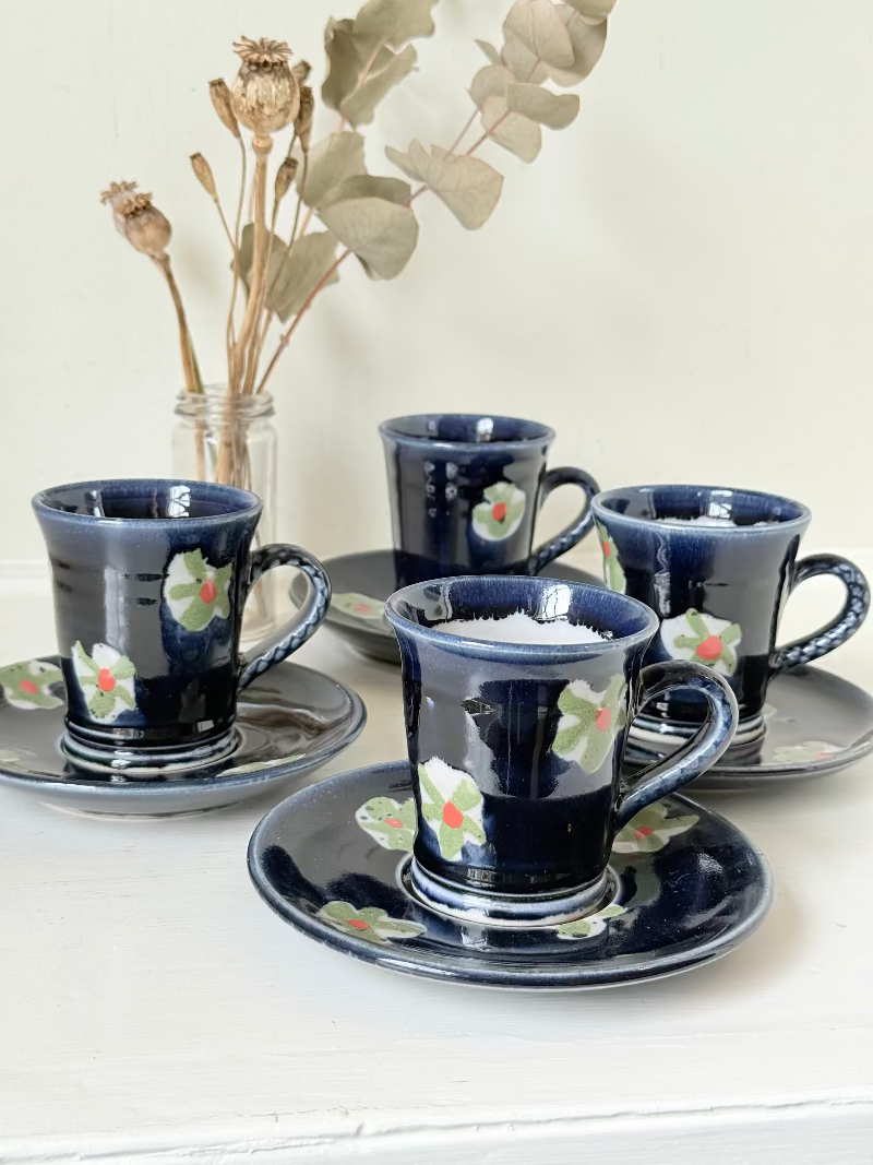 Vintage studio pottery coffee cans with matching saucers in navy glaze and floral motifs, set of four, photographed on a white surface