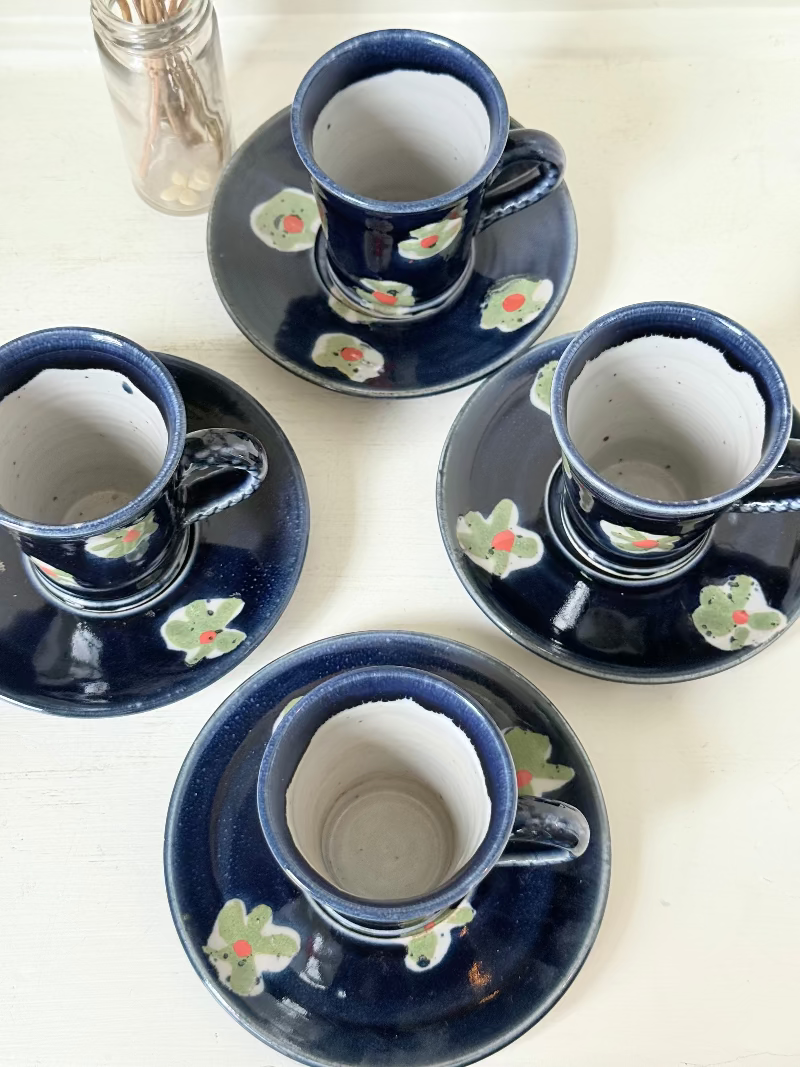 Vintage studio pottery coffee cans with matching saucers in navy glaze and floral motifs, set of four, photographed on a white surface