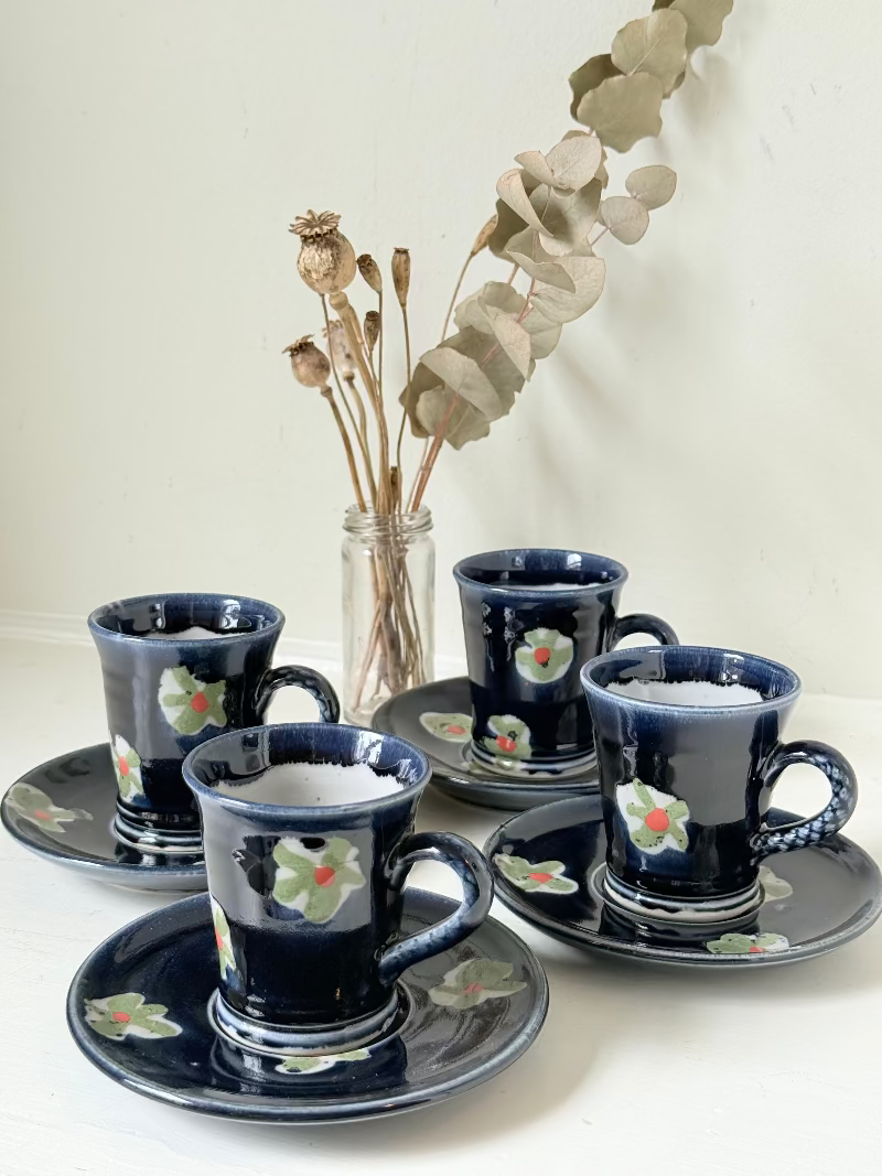 Vintage studio pottery coffee cans with matching saucers in navy glaze and floral motifs, set of four, photographed on a white surface