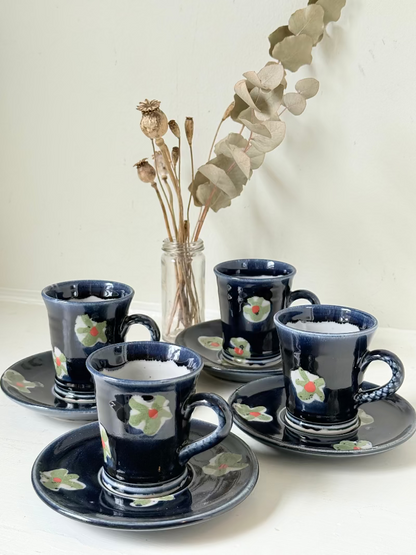 Vintage studio pottery coffee cans with matching saucers in navy glaze and floral motifs, set of four, photographed on a white surface
