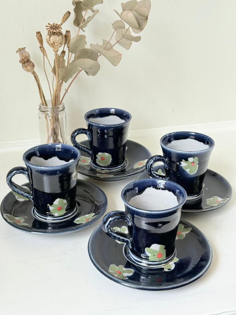 Vintage studio pottery coffee cans with matching saucers in navy glaze and floral motifs, set of four, photographed on a white surface
