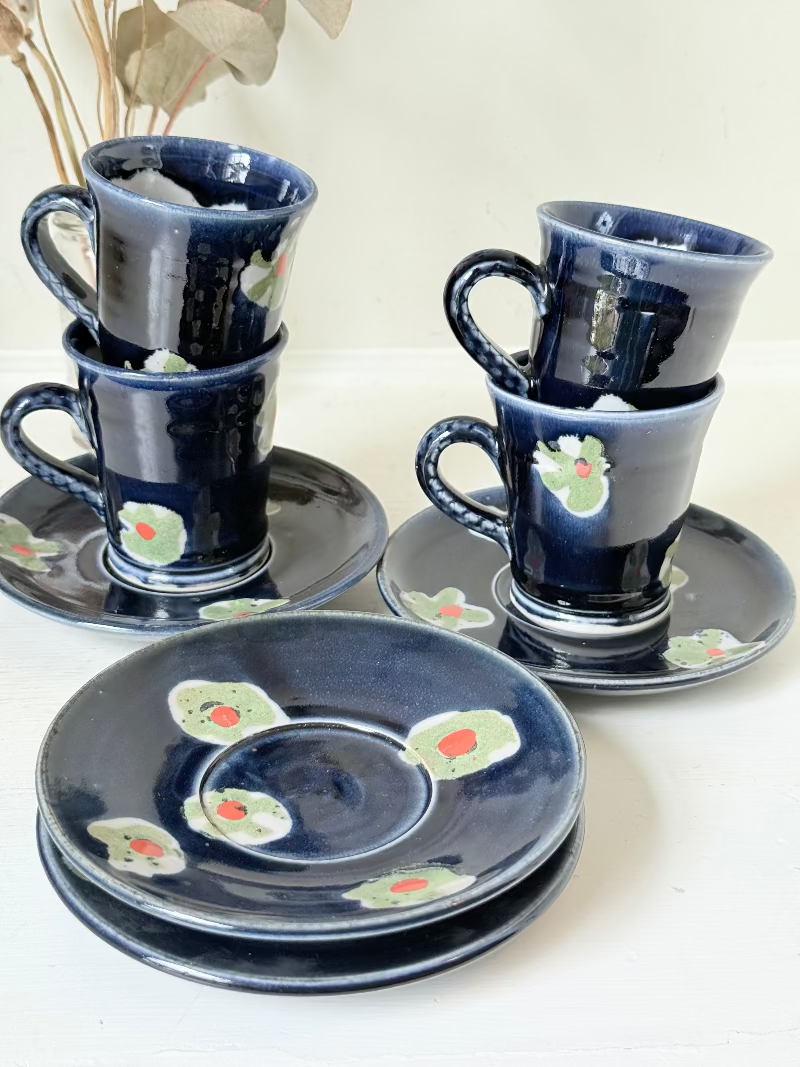 Vintage studio pottery coffee cans with matching saucers in navy glaze and floral motifs, set of four, photographed on a white surface