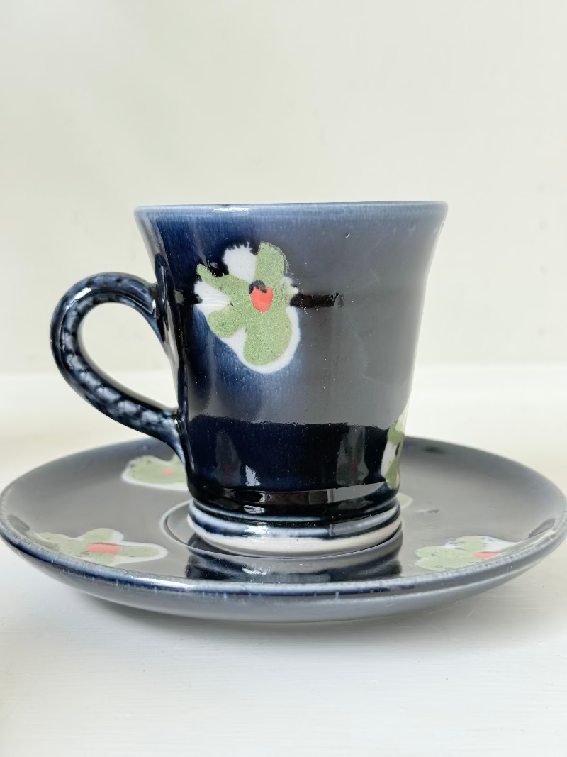 Vintage studio pottery coffee cans with matching saucers in navy glaze and floral motifs, set of four, photographed on a white surface