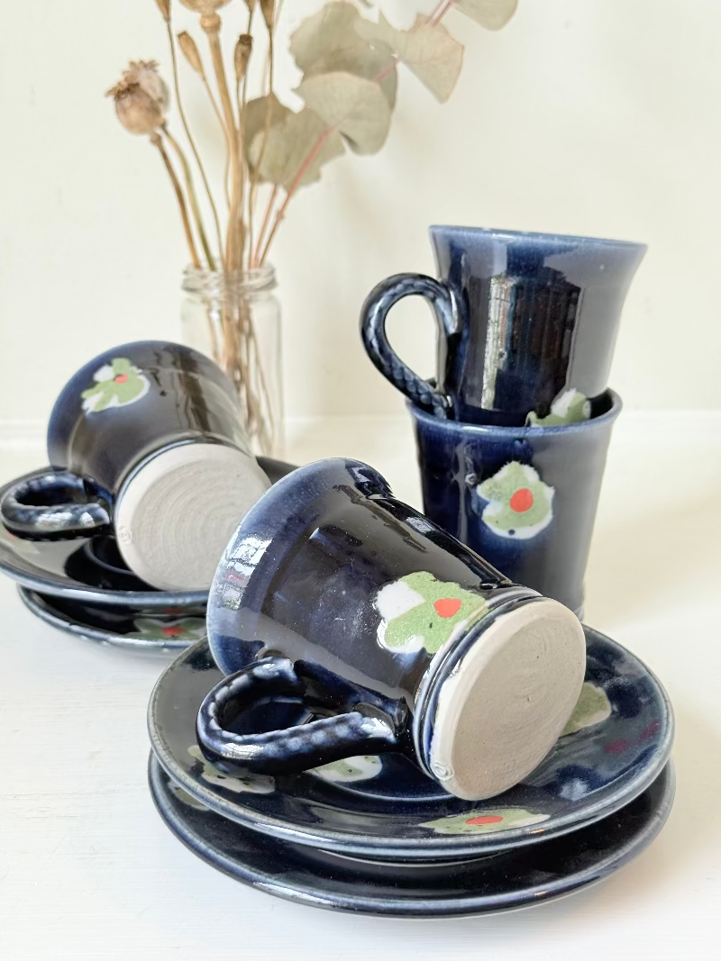 Vintage studio pottery coffee cans with matching saucers in navy glaze and floral motifs, set of four, photographed on a white surface