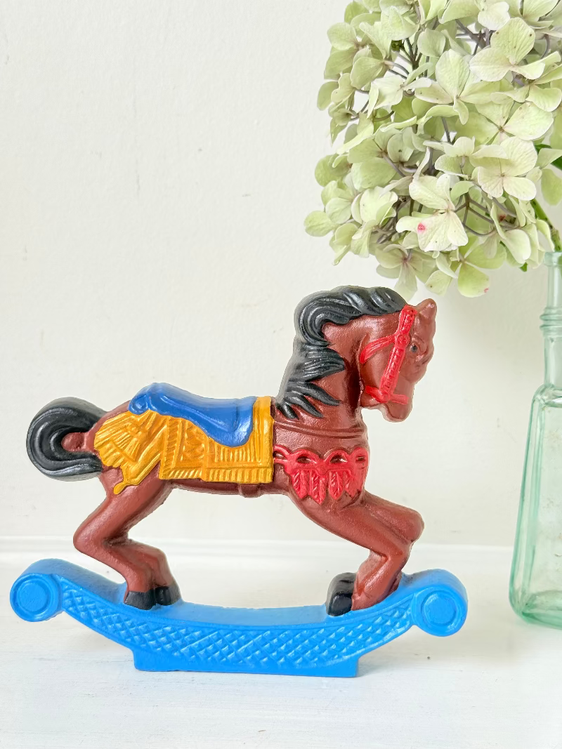 Vintage cast iron rocking horse doorstop with painted finish in red, yellow, blue, and black, photographed on a white surface