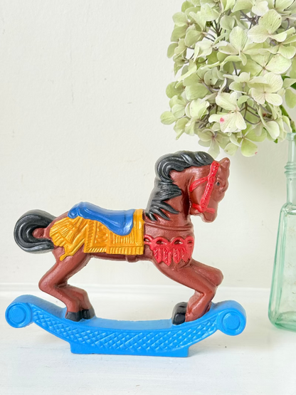 Vintage cast iron rocking horse doorstop with painted finish in red, yellow, blue, and black, photographed on a white surface