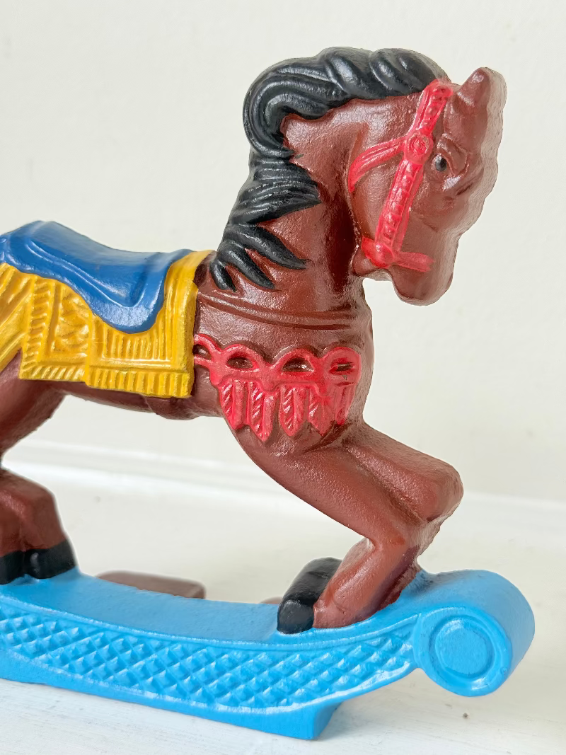 Vintage cast iron rocking horse doorstop with painted finish in red, yellow, blue, and black, photographed on a white surface