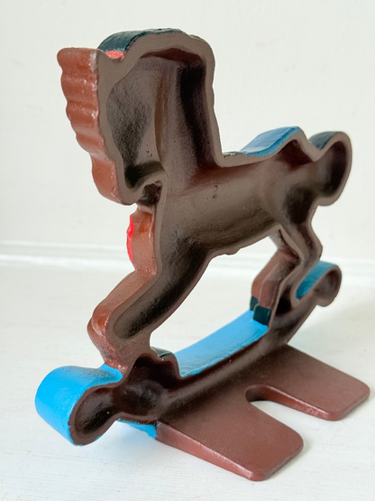 Vintage cast iron rocking horse doorstop with painted finish in red, yellow, blue, and black, photographed on a white surface