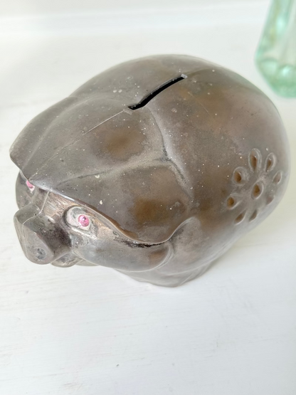 Vintage cast metal piggy bank in the shape of a pig with red painted eyes, photographed on a white surface