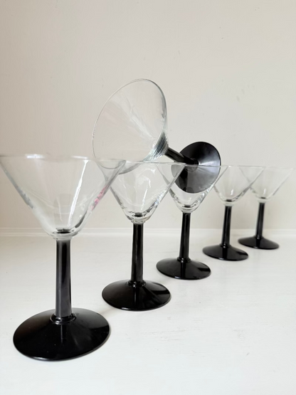 Set of six clear martini glasses with black stems, photographed on a white surface