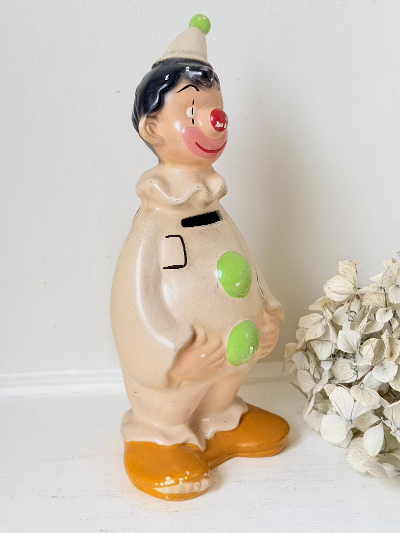 vintage ceramic clown moneybox with green and yellow painted details on white surface