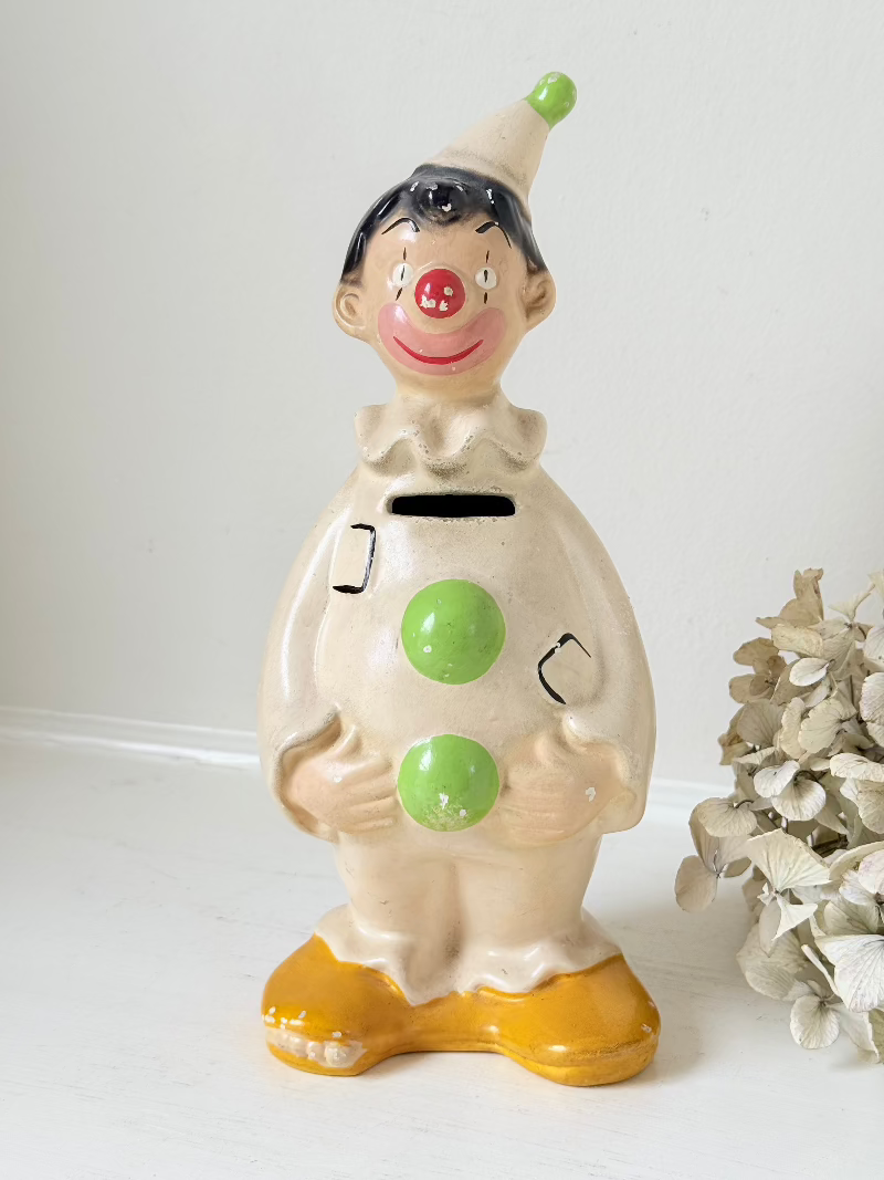 vintage ceramic clown moneybox with green and yellow painted details on white surface