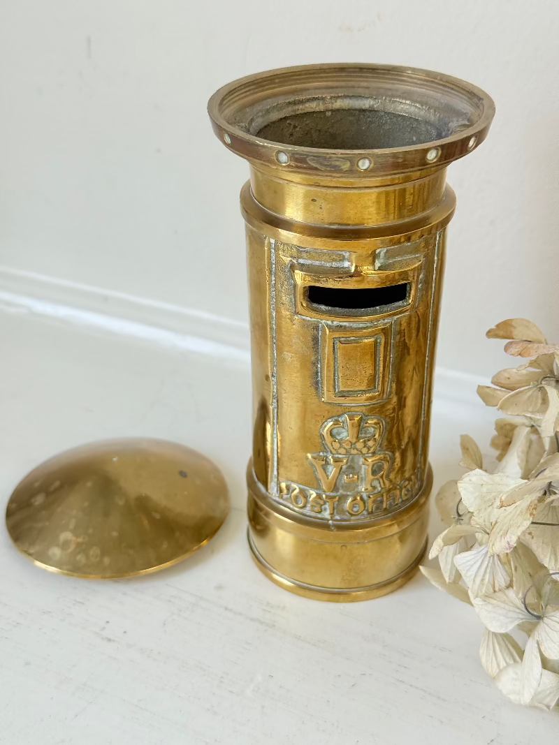 vintage brass post box moneybox with vr emblem photographed on white surface