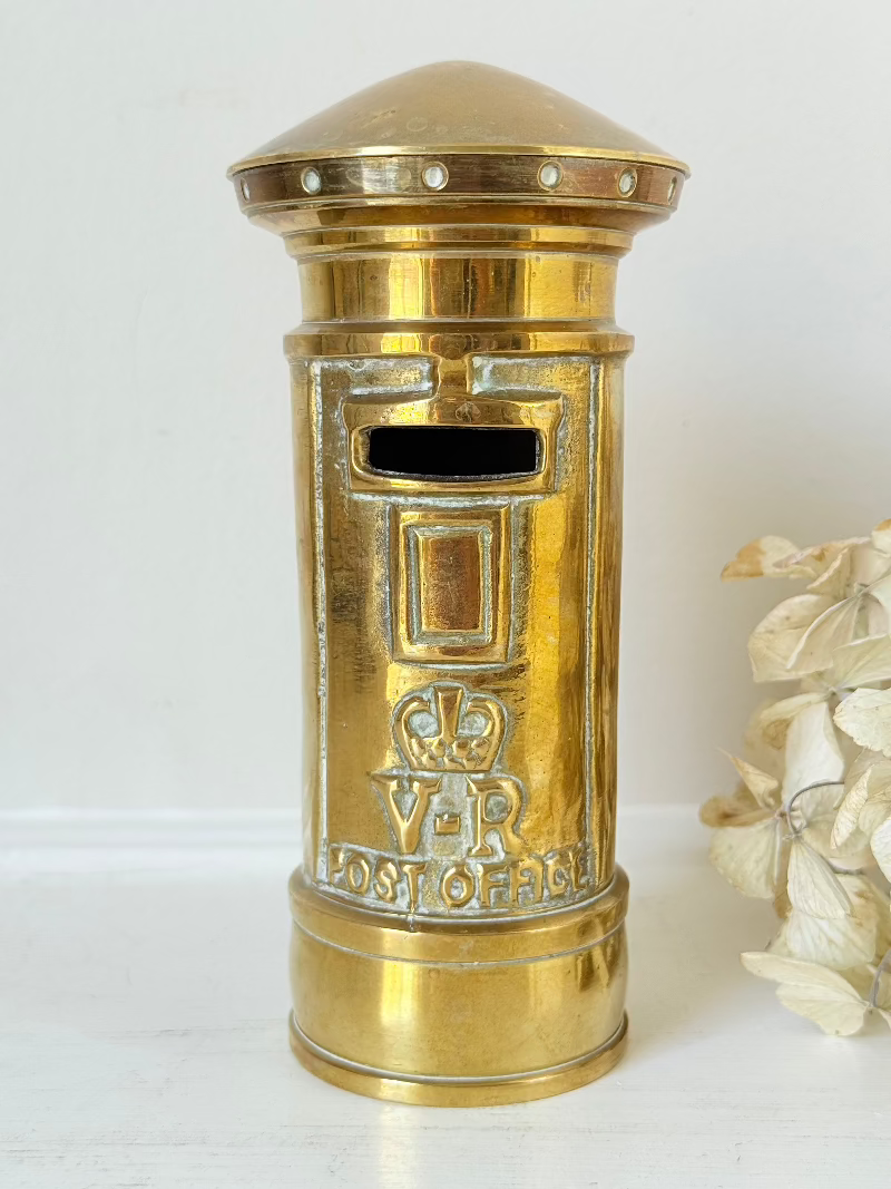 vintage brass post box moneybox with vr emblem photographed on white surface