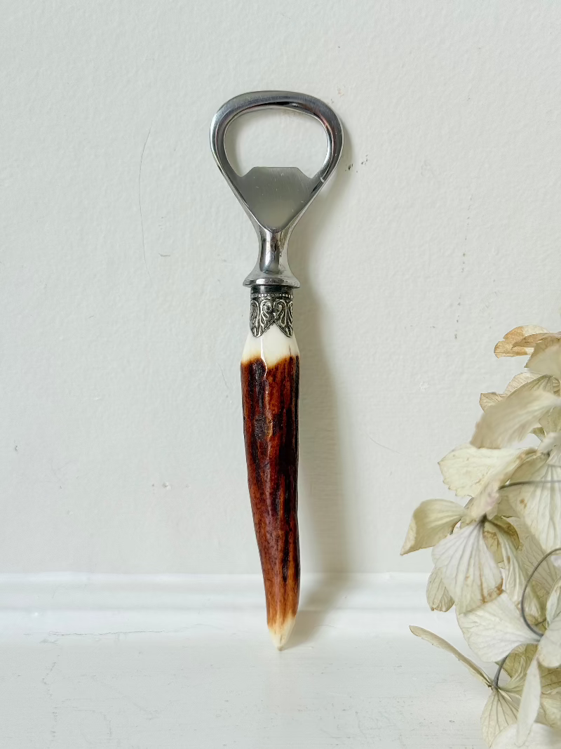 vintage antler handle bottle opener with stainless steel top photographed on white surface