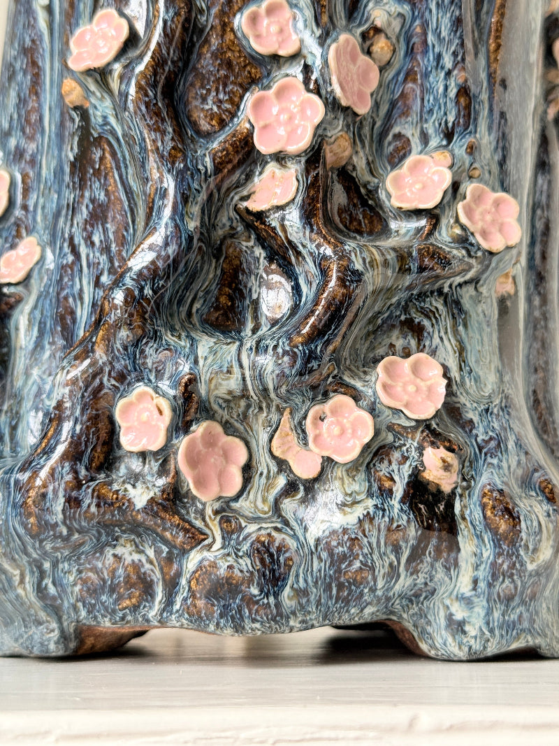 Large ceramic tree trunk vase with applied pink cherry blossom detail, textured bark form and dark drip glaze