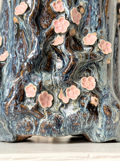Large ceramic tree trunk vase with applied pink cherry blossom detail, textured bark form and dark drip glaze
