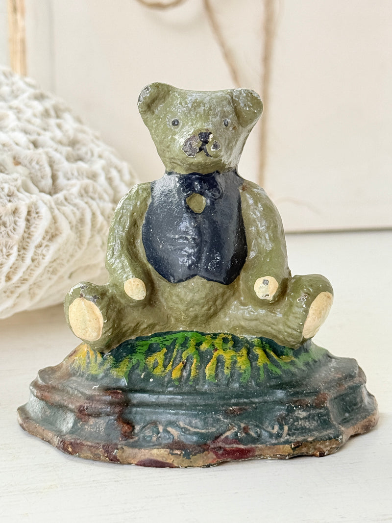 Vintage cast iron teddy bear doorstop in sage green with a navy waistcoat sitting on green grass