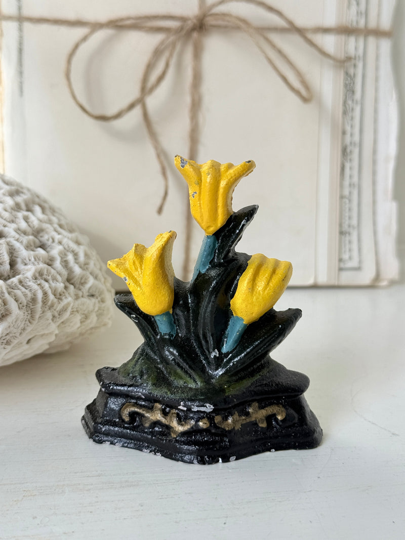 Yellow tulip cast iron doorstop on a white shelf in front of old books tied with string
