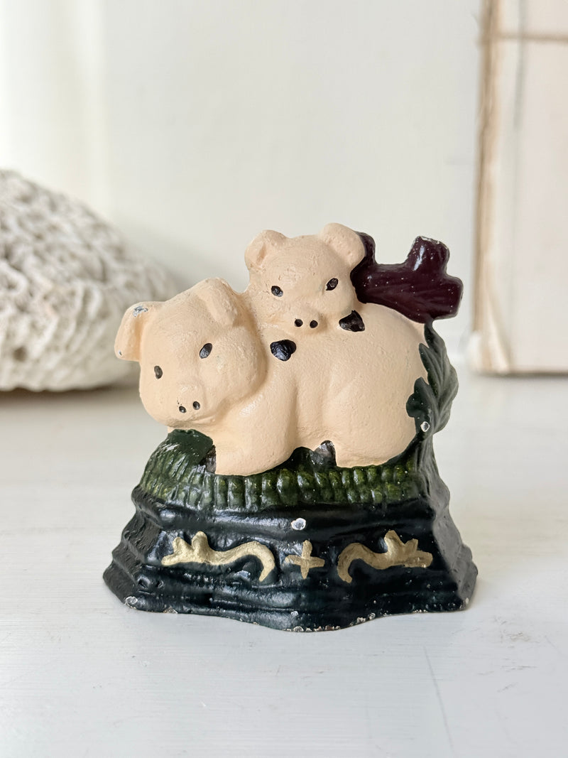 Vintage cast iron doorstop of two pink piglets snuggled on green grass on a black base with gold scrolls