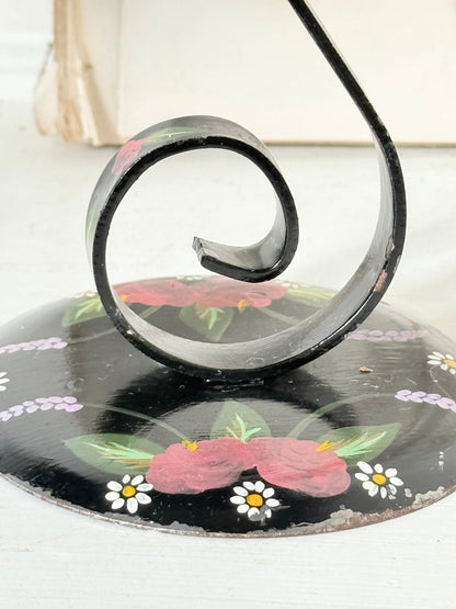 Scrolled stem of a vintage black toleware candlestick with painted roses